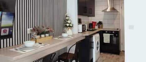 A modern kitchen with a central island, a washing machine, and a dining area with chairs.