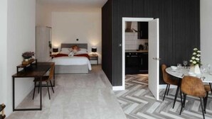 Una camera d'albergo moderna con un letto, un comodino e un'area pranzo con sedie e tavolo.
