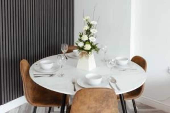 A round dining table with a white tablecloth, surrounded by brown chairs.
