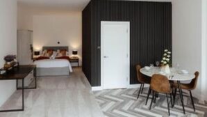 Una camera d'albergo moderna con un letto, un comodino, una lampada e un'area pranzo con sedie e tavolo.