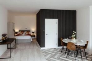 Ein modernes Hotelzimmer mit Bett, Nachttisch, Lampe und einem Essbereich mit Stühlen und Tisch.