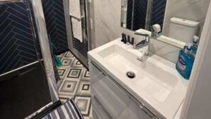 Un bagno con lavandino bianco, uno specchio, porta asciugamani e piastrelle decorative sul pavimento.