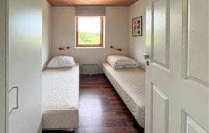 Een kleine kamer met twee bedden, een raam en een deur.