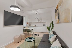 Una sala de estar moderna con una televisión de pantalla plana, un sofá, otomanas, una mesa de centro y un comedor con sillas y una mesa.