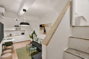 A modern kitchen with white cabinets, a dining area with a table and chairs, and a staircase with a wooden handrail. - [Vernazza Prestige] 5TERRE/ 10 mt the sea+A/C (Vernazza)