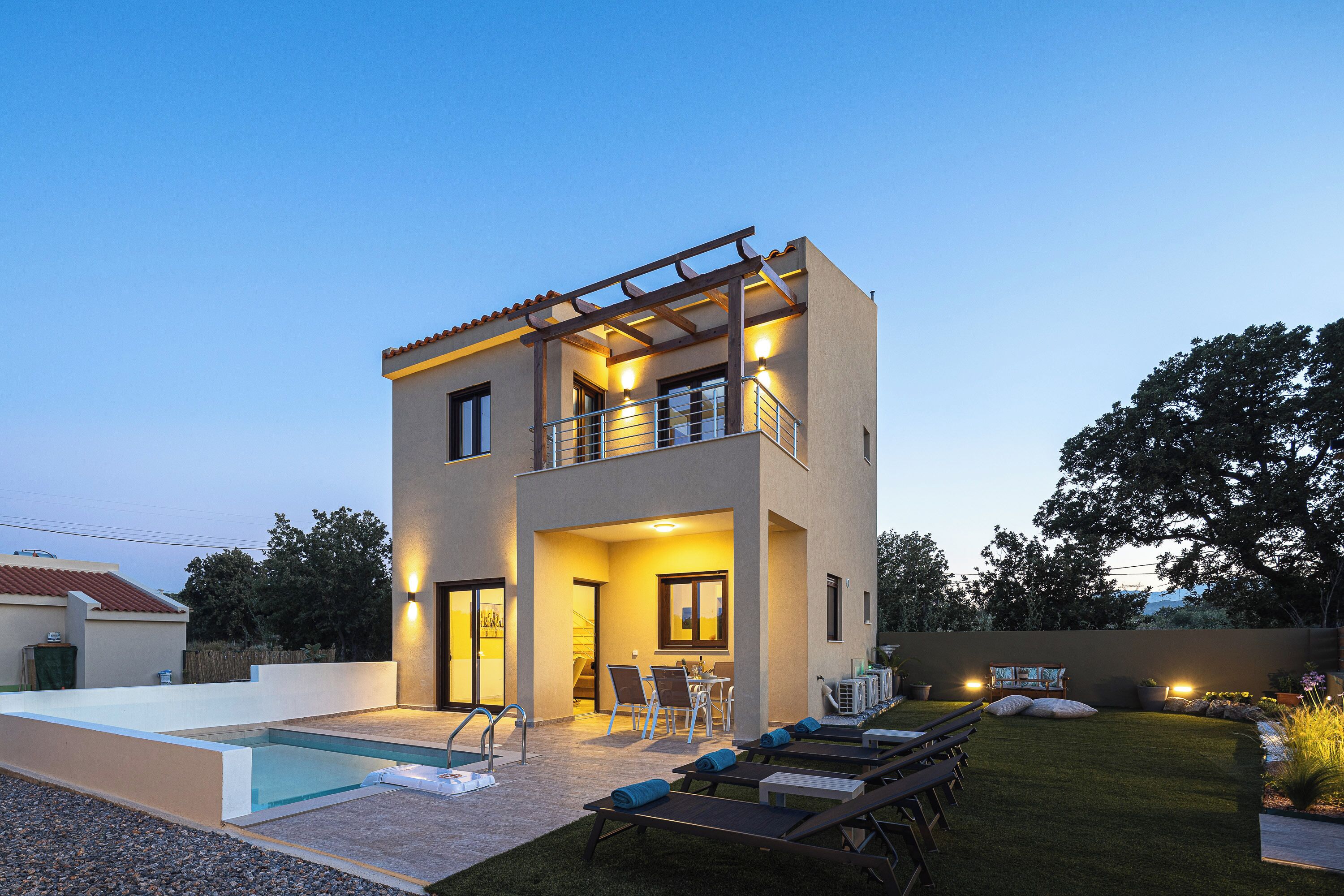 Una casa moderna de dos pisos con piscina, mobiliario exterior y un patio bien iluminado.