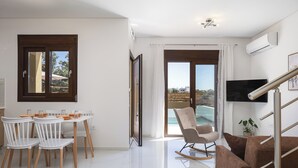 Un soggiorno moderno con zona pranzo, televisore montato a parete e vista attraverso la porta in vetro.