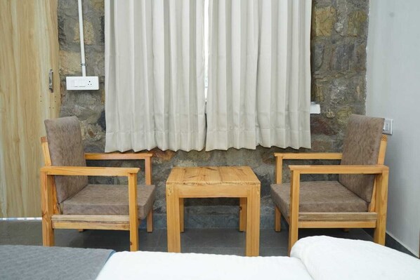 A room with two wooden chairs, a small wooden table, and a bed.