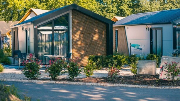 A modern, single-story building with a large glass window, a covered outdoor seating area, and a small garden with shrubs. - Holiday Home in Kaatsheuvel With Terrace (Kaatsheuvel)