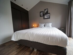 Ein Schlafzimmer mit einem großen Bett, dunklem Holzboden, einem Kleiderschrank und einer Wandleuchte.