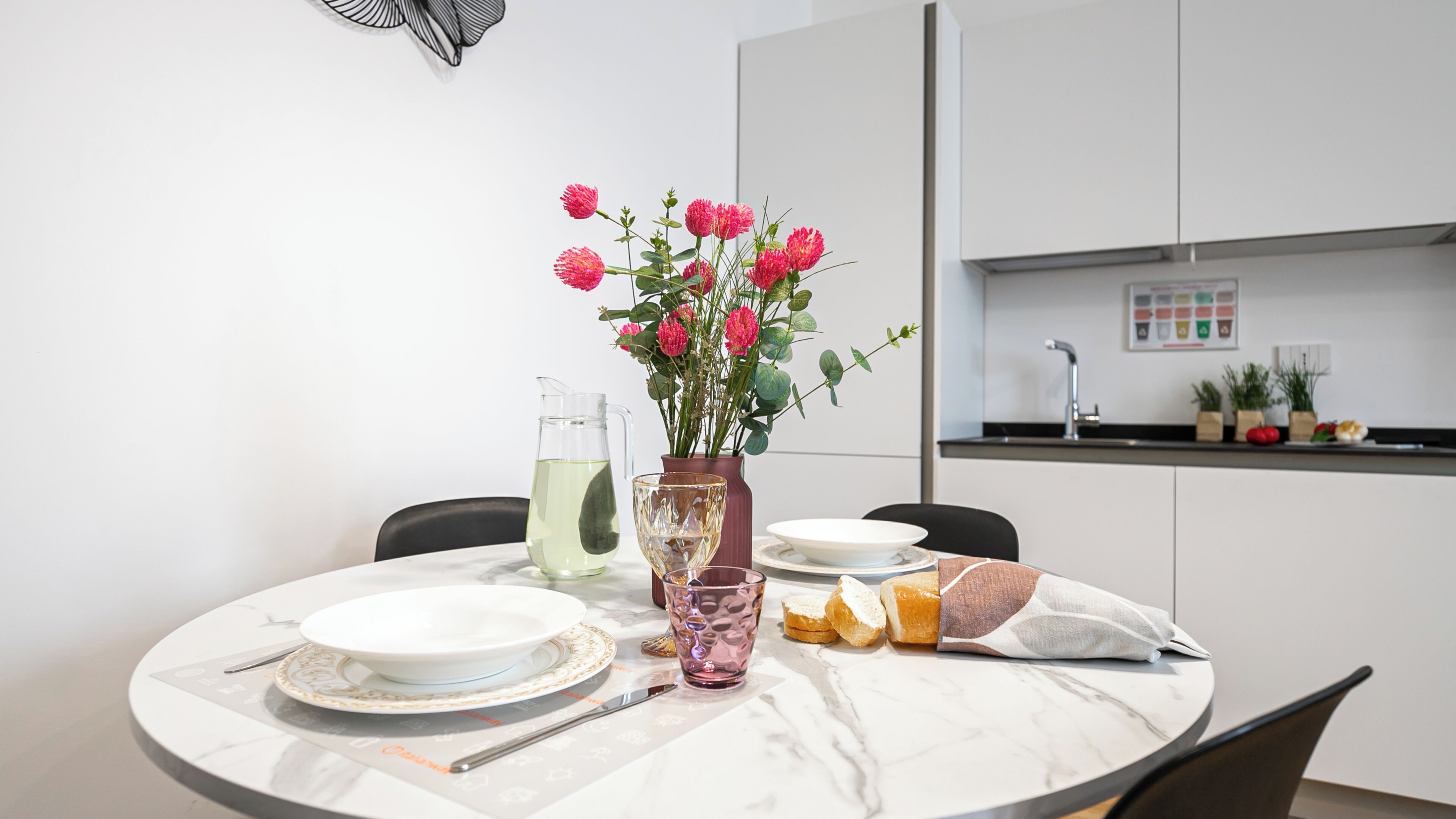 Ein Esstisch mit Tellern, einer Karaffe, einer Vase mit Blumen und einem Glas.