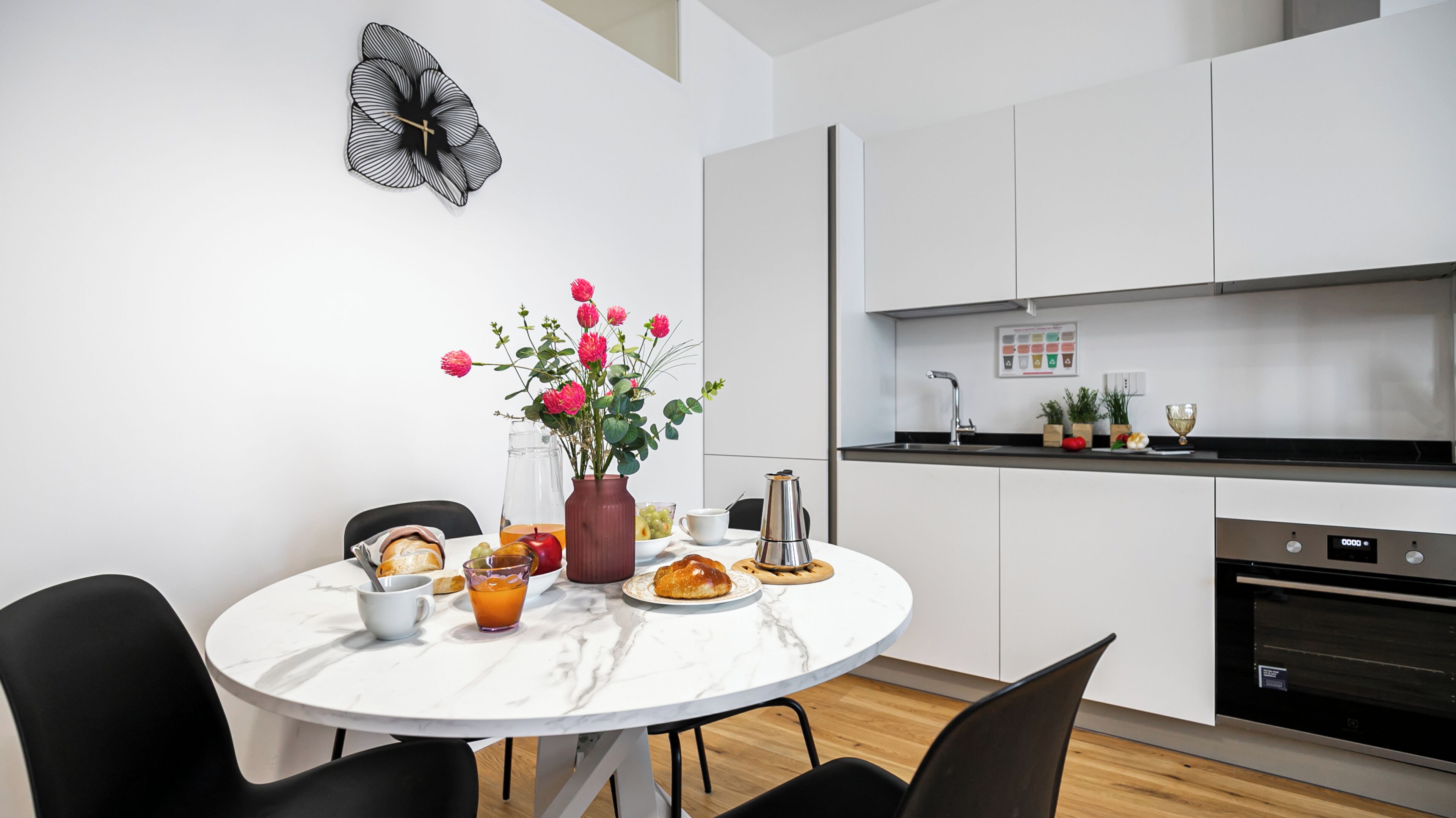 A modern kitchen with white cabinets, a marble dining table, and a vase of flowers.