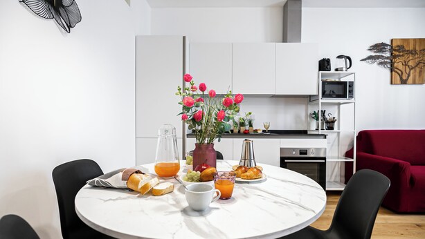 A modern kitchen with white cabinets, a dining table with a vase of flowers, and a red sofa. - Italianway Comfort - Boncompagni 3B (Milan)