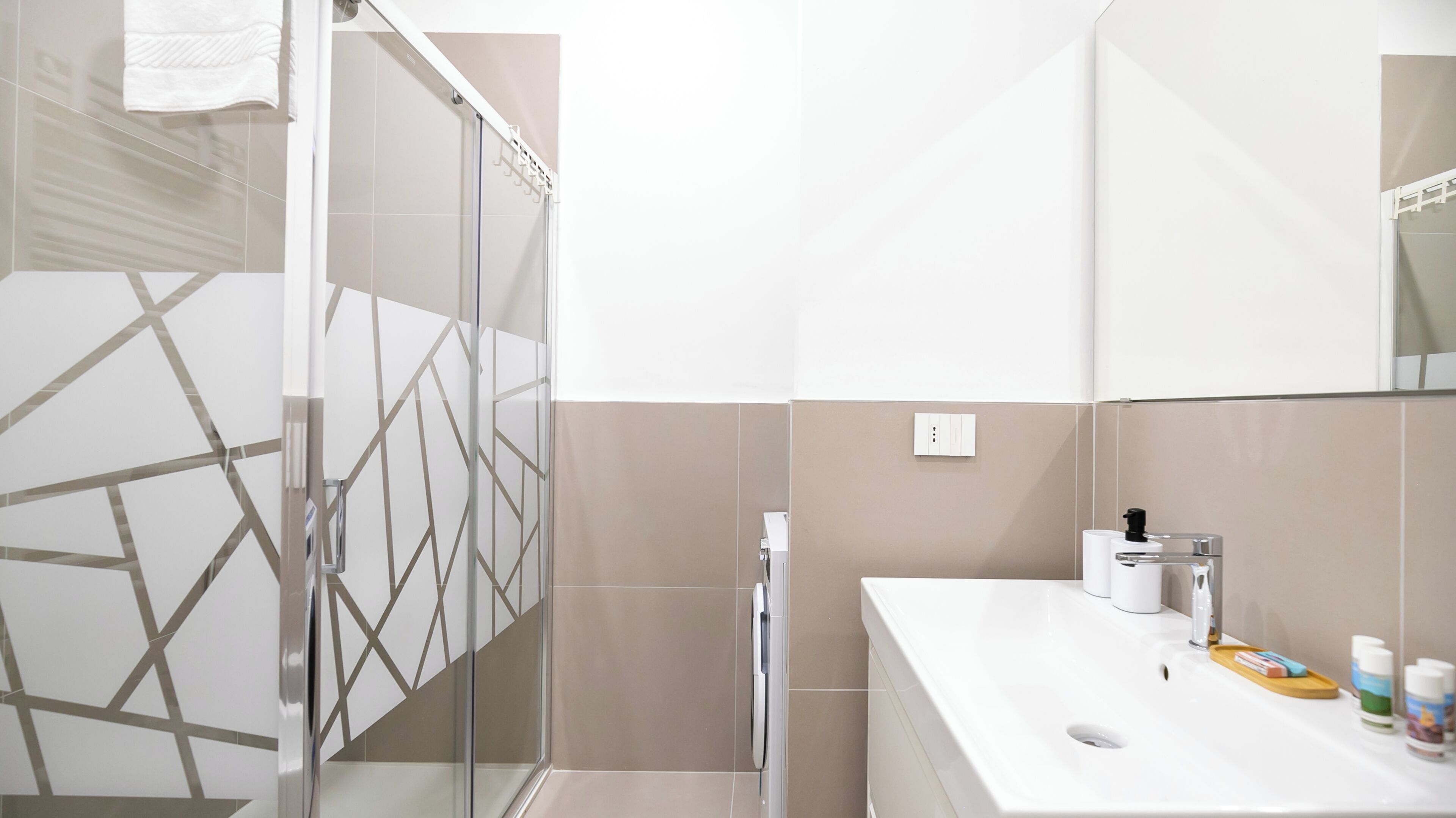 Een moderne badkamer met een douchecabine van glas, een witte wastafel met toiletartikelen en een grote spiegel.