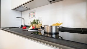 Una cuina moderna amb una olla d'acer inoxidable, una taula de tallar amb verdures i un tomàquet vermell.