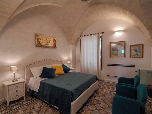 Une chambre à coucher avec un lit, des tables de chevet, une chaise, un radiateur et un tableau au mur.