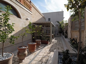 Un patio con plantas en macetas, suelo de baldosas y un edificio con ventana y balcón.