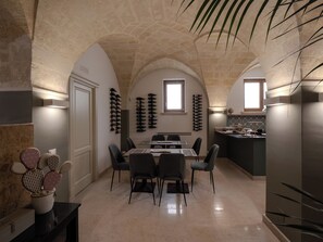 Un espace repas avec une table et des chaises, une cuisine à l’arrière-plan et un plafond en pierre.