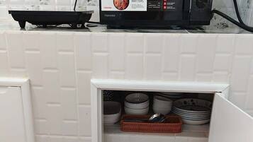 A compact kitchen with a microwave, a small refrigerator, and a storage cabinet containing dishes and jars.