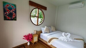 Ein Schlafzimmer mit einem Bett, Kissen, einem Nachttisch mit Blumen in einer Vase, einem Fenster und einem Gemälde an der Wand.