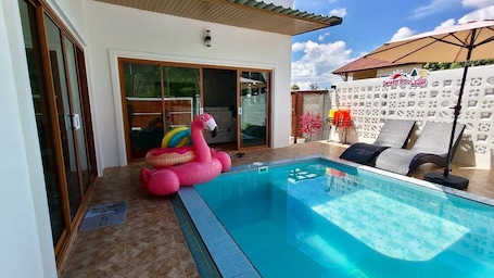 A swimming pool with a pink flamingo float, a covered seating area, and a sliding glass door leading to a room.