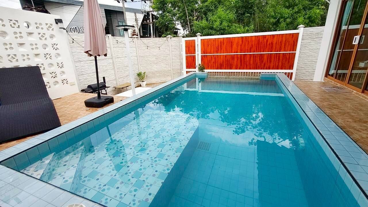 A rectangular swimming pool with tiled edges, a lounge chair, and a small table with an umbrella.
