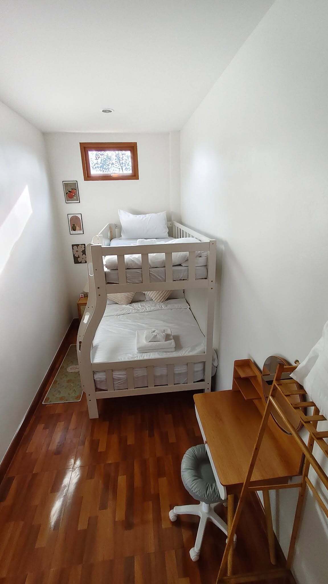 Una habitació petita amb parets blanques, un llit superposat, un escriptori i una cadira.