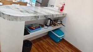 Una cocina con encimera de mármol, un lavamanos y una estufa. Hay cestas, un cubo de basura y un contenedor azul para guardar objetos.