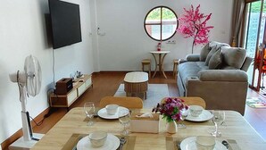 A dining area with a table set for four, a sofa, a TV, and a window with a view. - Selesa Pool Villa (Ban Phru)