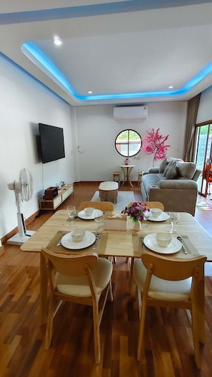 Un comedor con una mesa dispuesta para cuatro personas, un sofá, un televisor y una ventana con vistas.