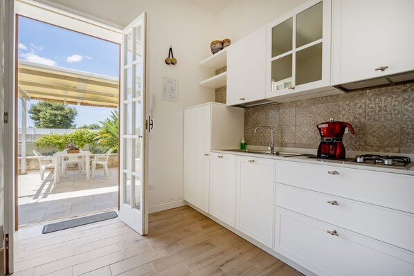 A kitchen with white cabinets, a red coffee maker, and a view of the outdoors. - This cozy apartment, perfect for two people, is located in a shared villa but has its own private access. It features a shared garden and a large furnished patio for exclusive use. The accommodation is located in Marina di Pulsano, a well-served seaside  (Marina di Pulsano)
