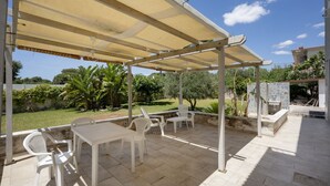 Um pátio externo com área de estar coberta, uma mesa e cadeiras.