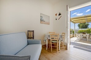A room with a sofa, a dining table with chairs, a picture on the wall, and a view through a glass door. - This cozy apartment, perfect for two people, is located in a shared villa but has its own private access. It features a shared garden and a large furnished patio for exclusive use. The accommodation is located in Marina di Pulsano, a well-served seaside  (Marina di Pulsano)