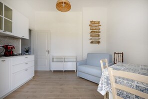A compact kitchen with white cabinetry, a red coffee maker, and a small island. There is a light blue sofa and a dining table with a patterned tablecloth. - This cozy apartment, perfect for two people, is located in a shared villa but has its own private access. It features a shared garden and a large furnished patio for exclusive use. The accommodation is located in Marina di Pulsano, a well-served seaside  (Marina di Pulsano)