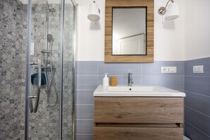 A bathroom with a glass shower enclosure, a wooden vanity with a mirror, and a white sink. - This cozy apartment, perfect for two people, is located in a shared villa but has its own private access. It features a shared garden and a large furnished patio for exclusive use. The accommodation is located in Marina di Pulsano, a well-served seaside  (Marina di Pulsano)
