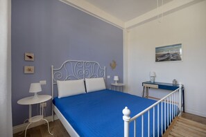 A bedroom with a bed, a desk, a chair, a lamp, and a wall-mounted artwork. - This cozy apartment, perfect for two people, is located in a shared villa but has its own private access. It features a shared garden and a large furnished patio for exclusive use. The accommodation is located in Marina di Pulsano, a well-served seaside  (Marina di Pulsano)