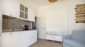 Cozinha moderna com armários brancos, uma cafeteira vermelha e uma placa de madeira com destinos litorâneos.