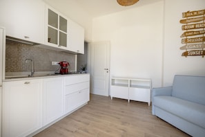 A modern kitchen with white cabinets, a red coffee maker, and a wooden sign with coastal destinations. - This cozy apartment, perfect for two people, is located in a shared villa but has its own private access. It features a shared garden and a large furnished patio for exclusive use. The accommodation is located in Marina di Pulsano, a well-served seaside  (Marina di Pulsano)