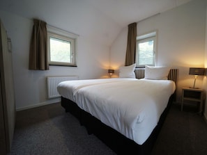 A hotel room with a large bed, two bedside tables with lamps, a radiator, and two windows with curtains. - Secret van Otterlo Luxe 10 (Otterlo)