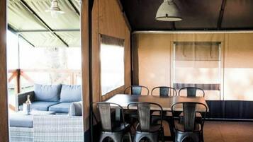 A covered outdoor dining area with a table and chairs, a sofa, and a hanging light fixture.