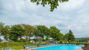 En swimmingpool med blå solstolar, en gräsyta och träd i bakgrunden.