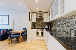 A modern kitchen with white cabinets, a black countertop, and a tiled backsplash. - Inviting 1BDR Flat in Earls Court (Greater London)