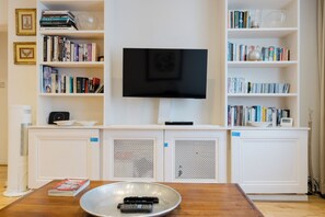 A living room with a flat-screen TV mounted on the wall, surrounded by bookshelves filled with books. - Inviting 1BDR Flat in Earls Court (Greater London)