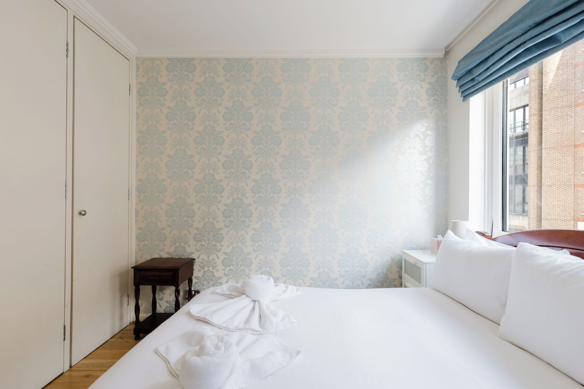 Una habitación de hotel con una cama, una mesita de noche, una pequeña mesa y una ventana con cortinas.