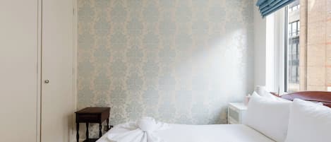 A hotel room with a bed, a nightstand, a small table, and a window with curtains.