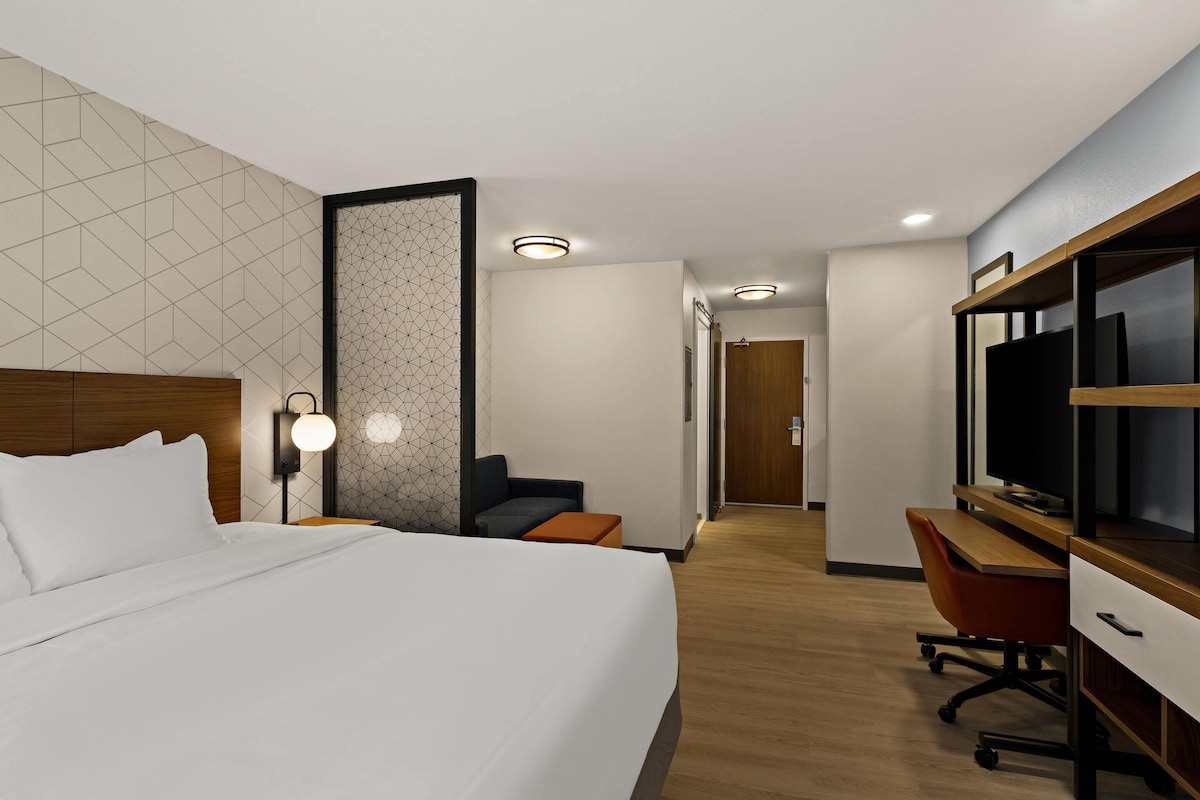 A hotel room with a bed, a desk, a TV, and a seating area.