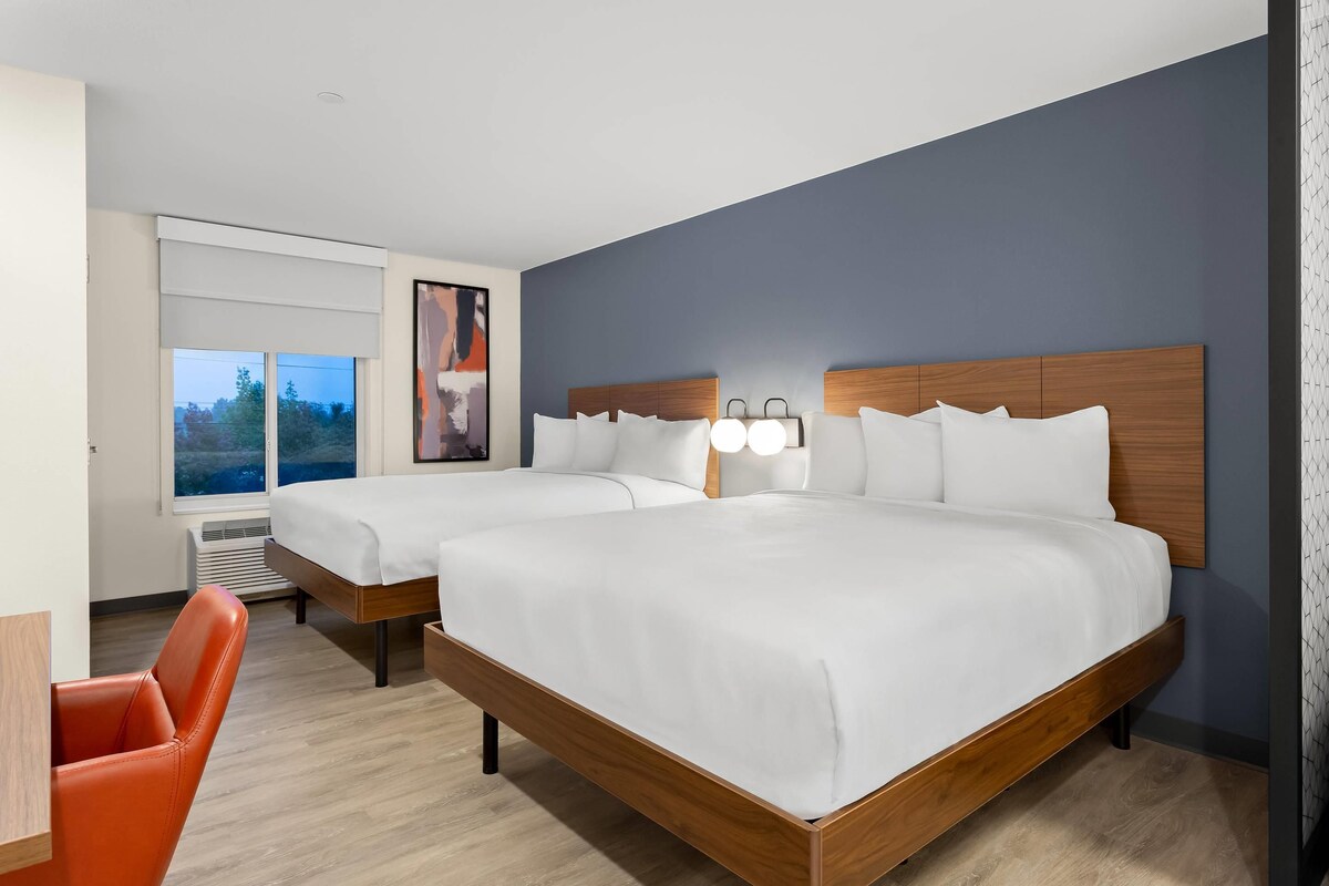 A hotel room with two beds, a desk, and a chair.