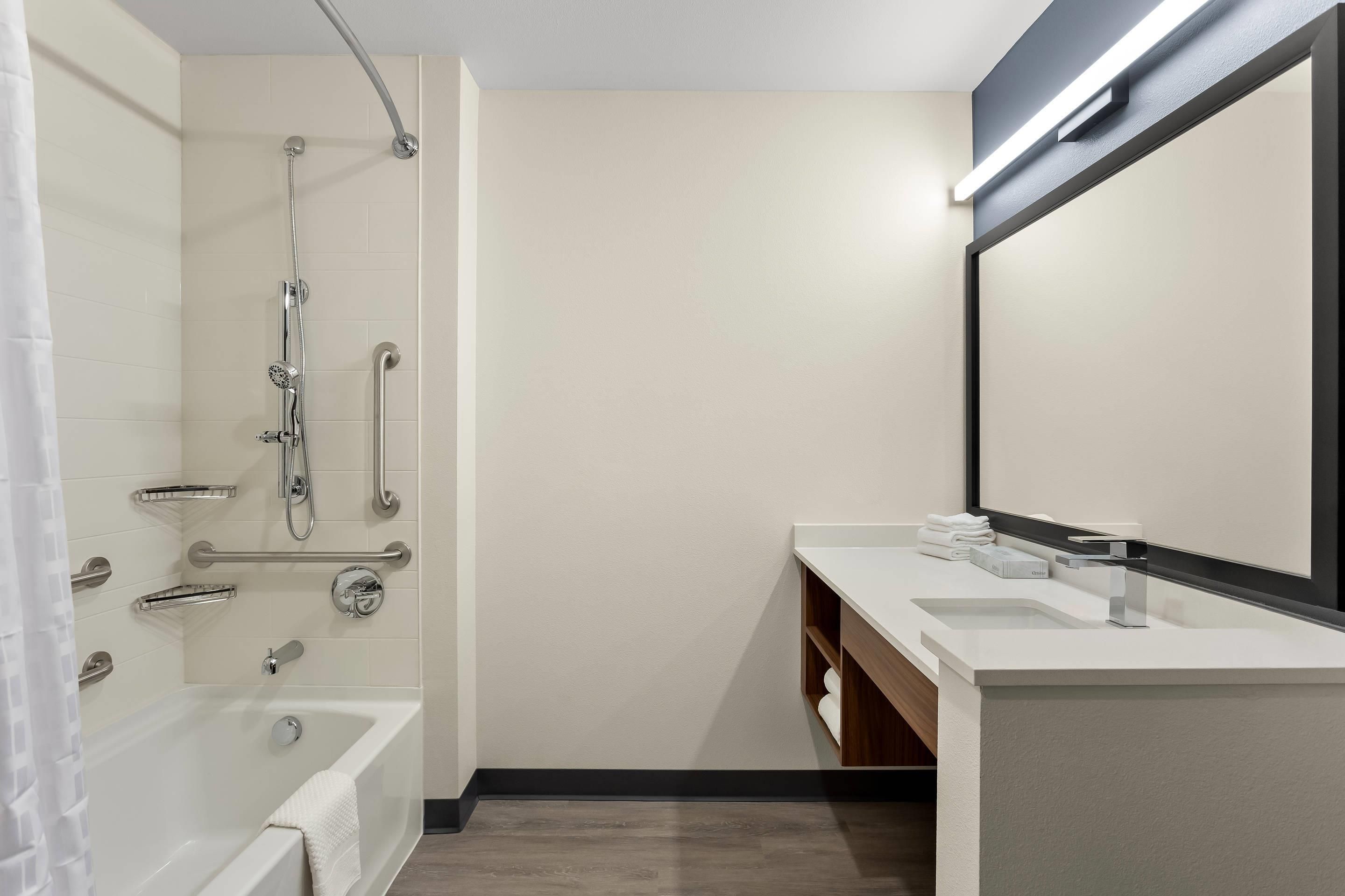 A modern bathroom with a bathtub, a shower with grab bars, a vanity with a mirror, and a towel rack.