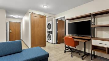 A modern bedroom with a bed, a desk with a computer, a TV, and a washing machine.