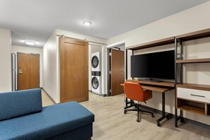 Un dormitorio moderno con cama, escritorio con computadora, televisor y lavadora.